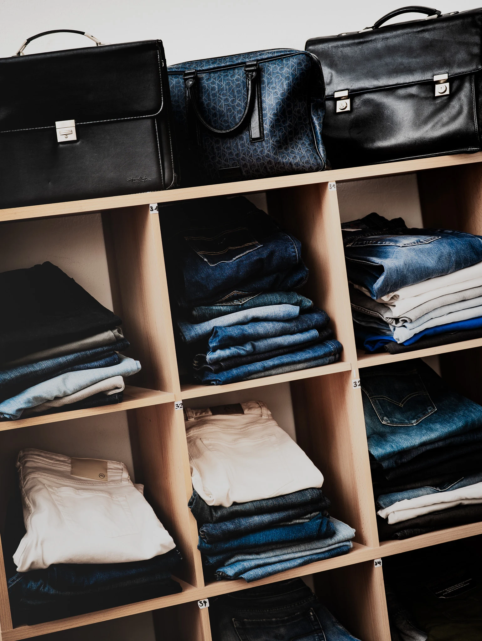 Aktentaschen aus Leder und gefaltete Jeans im Regal
